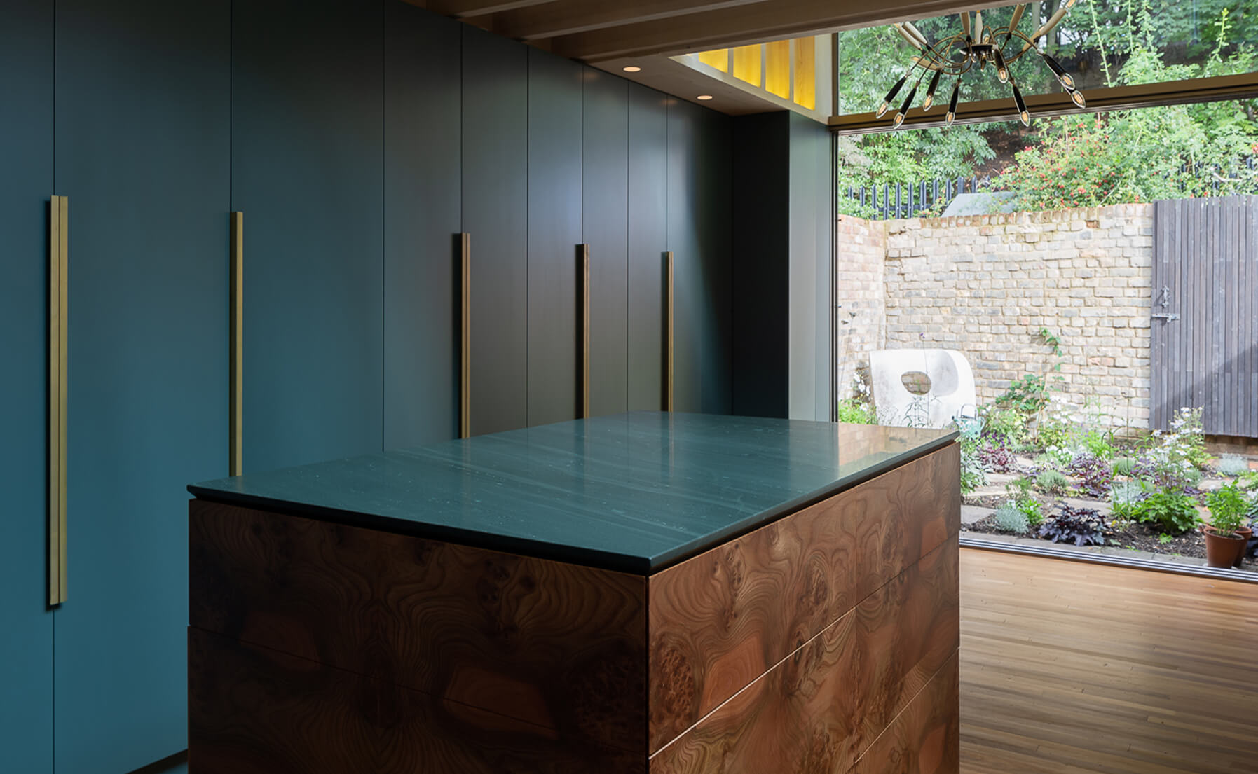 Modern kitchen with slate stone island countertop and blue cabinetry, featuring natural wood accents and large window overlooking a garden.